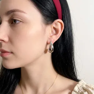 Polished silver teardrop C-shape hoop earrings worn by a model in a minimalist style