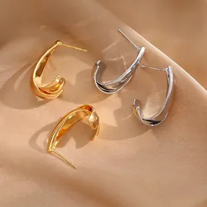 Minimalist gold and silver twisted C-shape earrings on elegant champagne silk