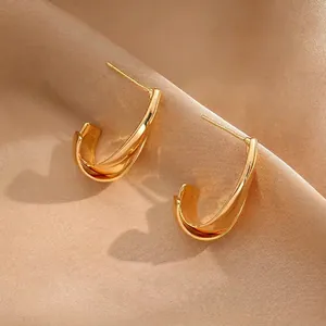 Macro shot of gold-plated curved wide hoop earrings on a luxury champagne satin background