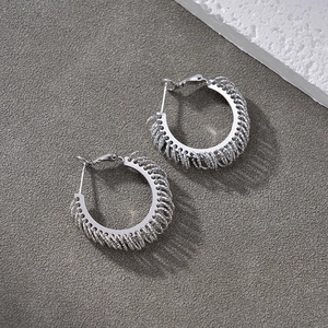 Detail of silver hoop earrings with intricate metallic woven texture on stone background