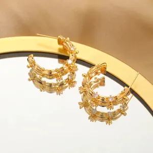 Macro shot of gold C-shaped hoop earrings with zircons on a mirrored surface