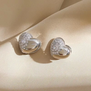 Macro shot of silver heart earrings with white cubic zirconia on champagne silk background