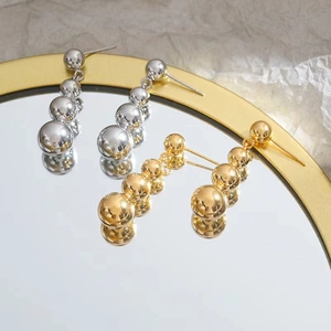 Elegant long metal ball drop earrings in gold and silver finish on mirror background