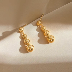 Detail of elegant gold drop earrings with polished metal spheres on silk fabric