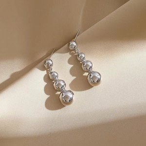 Detail of silver drop earrings with four gradient metal spheres on silk fabric