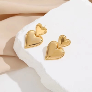 Close-up of golden double heart earrings on a white stone base with soft fabric background