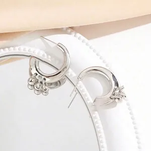 Minimalist silver C-shape hoop earrings with polished metal bead pendants on white tray