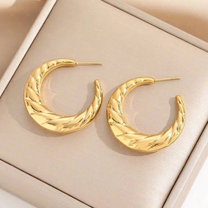 Golden chunky croissant hoop earrings in twisted metal texture on silk background