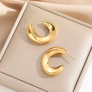 Close-up of chunky gold C-shaped earrings with a high-polished metallic mirror finish