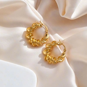 Elegant gold twisted hoop earrings with textured finish on champagne silk background