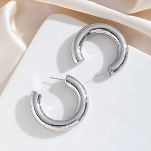 Detailed close-up of large chunky silver-finish C-shape hoop earrings on elegant satin