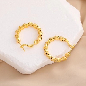 Gros plan de créoles torsadées plaquées or 18 carats sur un support en pierre chic