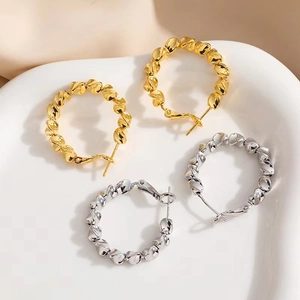 Boucles d'oreilles créoles torsadées dorées et argentées sur un plateau blanc