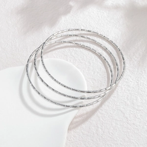 Détail de trois bracelets joncs fins en acier inoxydable argenté avec motifs gravés