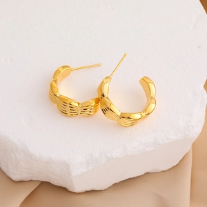 Detail of 18K gold-plated C-shaped hoop earrings with textured fan patterns on a white stone