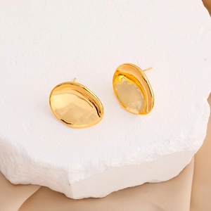 Irregular glossy oval gold petal stud earrings on white stone slab with warm lighting