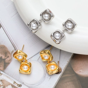 Detail of elegant gold and silver square frame stud earrings with central pearls on a tray