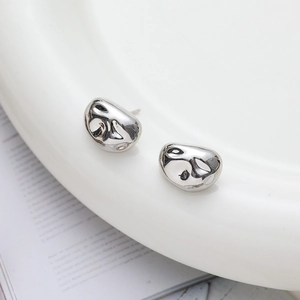 Minimalist silver organic pebble earrings with high-polish mirror finish on a ceramic plate