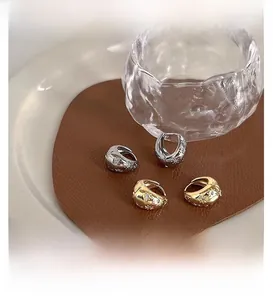 Close-up of gold and silver oval hoop earrings with star pattern and zircons on leather