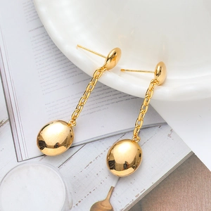 Elegant gold drop earrings with polished oval pendants on a white porcelain dish