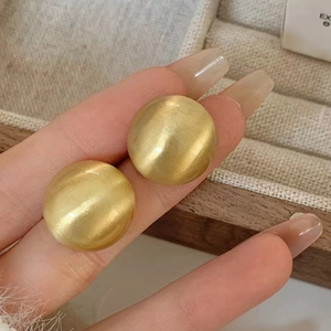 Boucles d'oreilles boules dorées brossées élégantes avec finition métallique mate en main