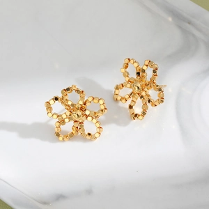 Boucles d'oreilles fleur dorées avec pétales perlés sur fond de marbre blanc