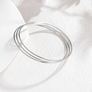 Détail de trois joncs minimalistes en acier inoxydable argenté sur un plateau blanc