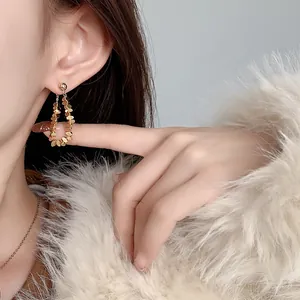 Detail of gold sequin tassel earrings in a teardrop shape on a model with fur coat