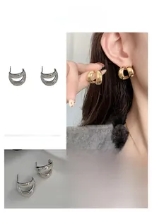 Detailed view of layered C-shaped earrings in polished gold and silver metallic finishes