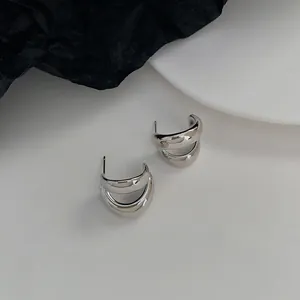 Detail of silver double-layered C-shaped earrings on a white plate and black paper