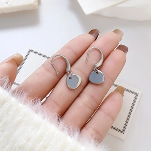 Minimalist hook earrings in polished silver metal with irregular flat disc pendants