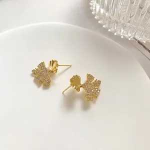 Elegant gold ginkgo leaf stud earrings with pavé diamonds on a minimalist white plate