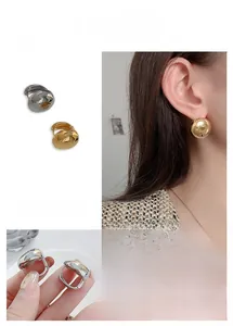 Macro detail of bean-shaped gold and silver earrings showing a mirror finish and clasp