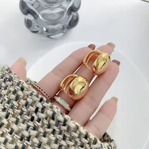 Detailed close-up of golden dome stud earrings with a polished mirror finish on a ceramic plate