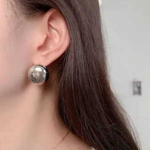 Polished silver sphere stud earrings with a glossy mirror finish on a female model