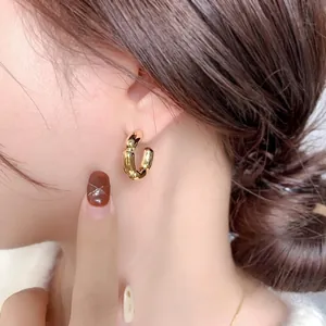 Boucles d'oreilles créoles C en or 18 carats style bambou portées par un mannequin élégant