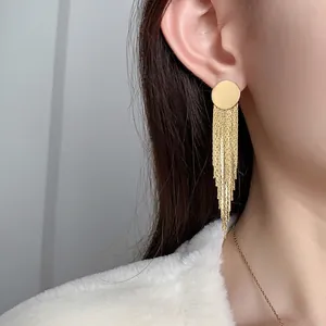 Elegant gold fringe tassel earrings with round geometric studs worn on a model's ear