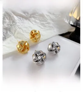 Detail of 18K gold and silver plated woven knot stud earrings on white display surface