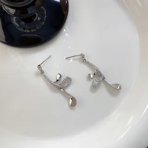 Detail of silver leaf-shaped earrings with micro-set zircons on white plate