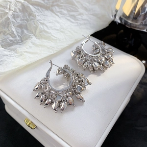 Detailed close-up of silver C-shape earrings with hanging heart charms on jewelry box