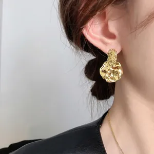 Irregular gold-plated dangle earrings with hammered texture on a female model