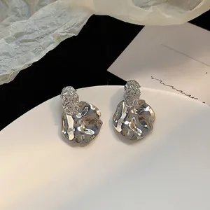 Detailed close-up of silver irregular pleated metal earrings with fluid metallic texture