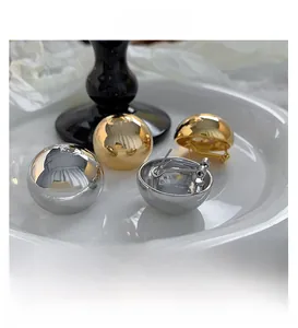 Macro shot of minimalist gold and silver polished dome earrings on a white ceramic tray