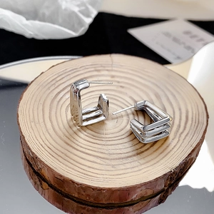 Détail macro de boucles d'oreilles carrées triples en argent sur socle bois