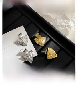 Detailed view of gold and silver textured triangle drop earrings on a jewelry tray