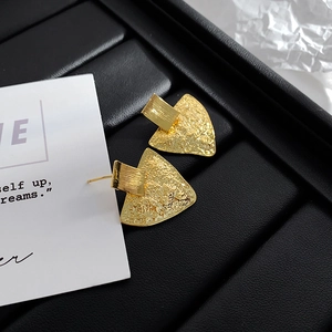 Macro detail of gold geometric earrings with a unique hammered texture on black leather