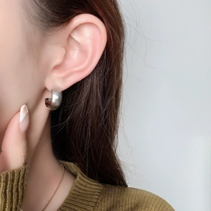 Minimalist C-shaped silver brushed metal hoop earrings worn by a model in a close-up view