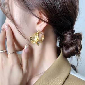 Elegant gold flower stud earrings with hammer-textured petals and center pearl on a model