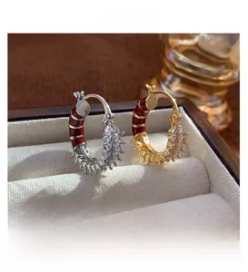 Macro detail of vintage gold and silver C-shaped earrings with red enamel and zircons