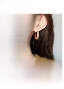 Detail of gold-plated caterpillar hoop earrings with red enamel and zircon stones